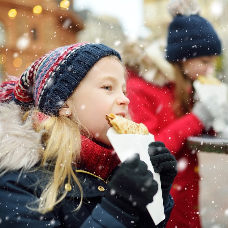 Young Girl Eating Crepe Under The Snow