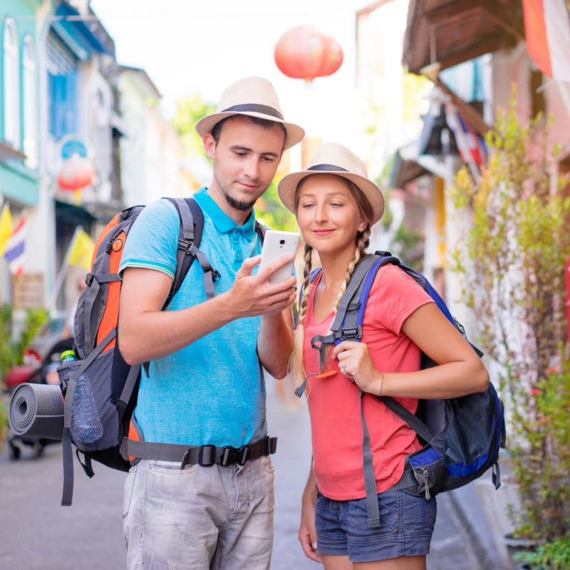 Man and woman backpackers standing in the street using their phone