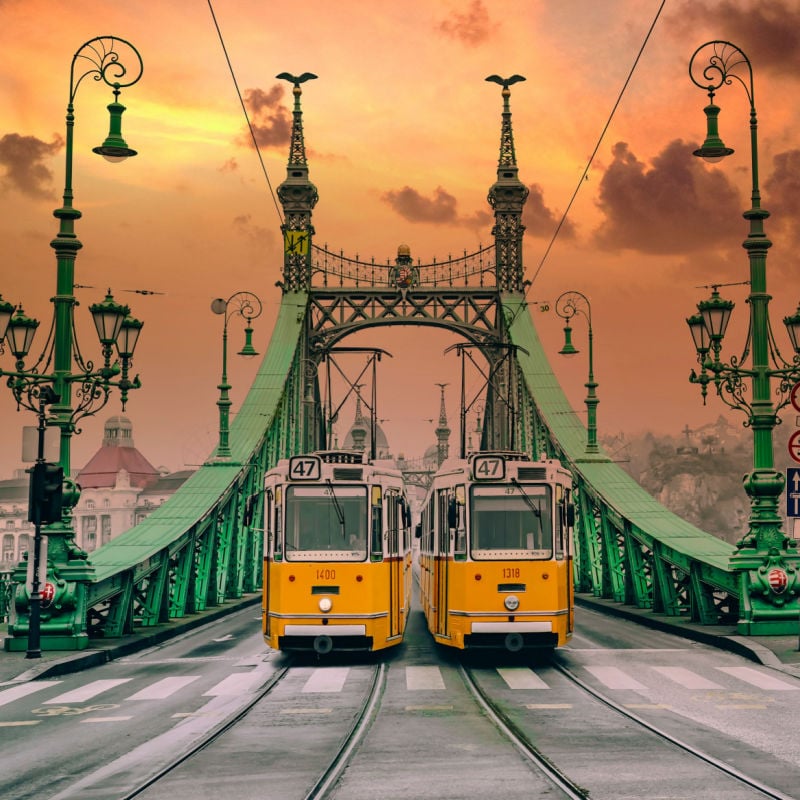 two yellow trams pass eachother while crossing a green bridge in Budapest