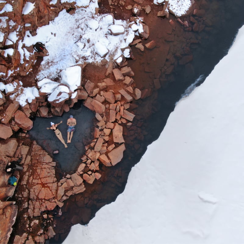 young couple warming up in hot spring in colorado in the snow