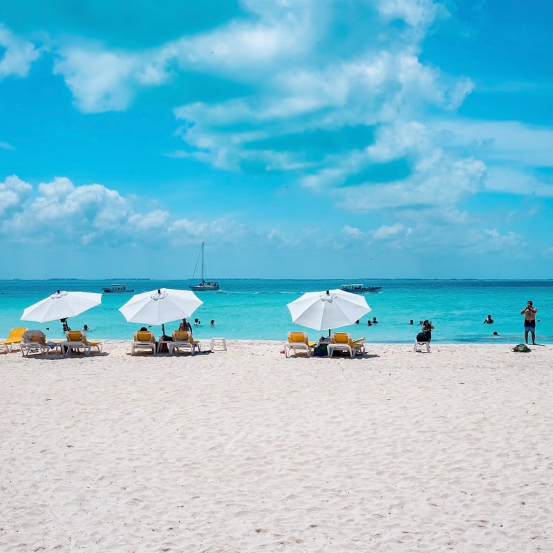 Cancun, Mexico. Deckchairs under canopy shade for resting on beach sand in front of sea with yachts. Tourists enjoying beach holiday