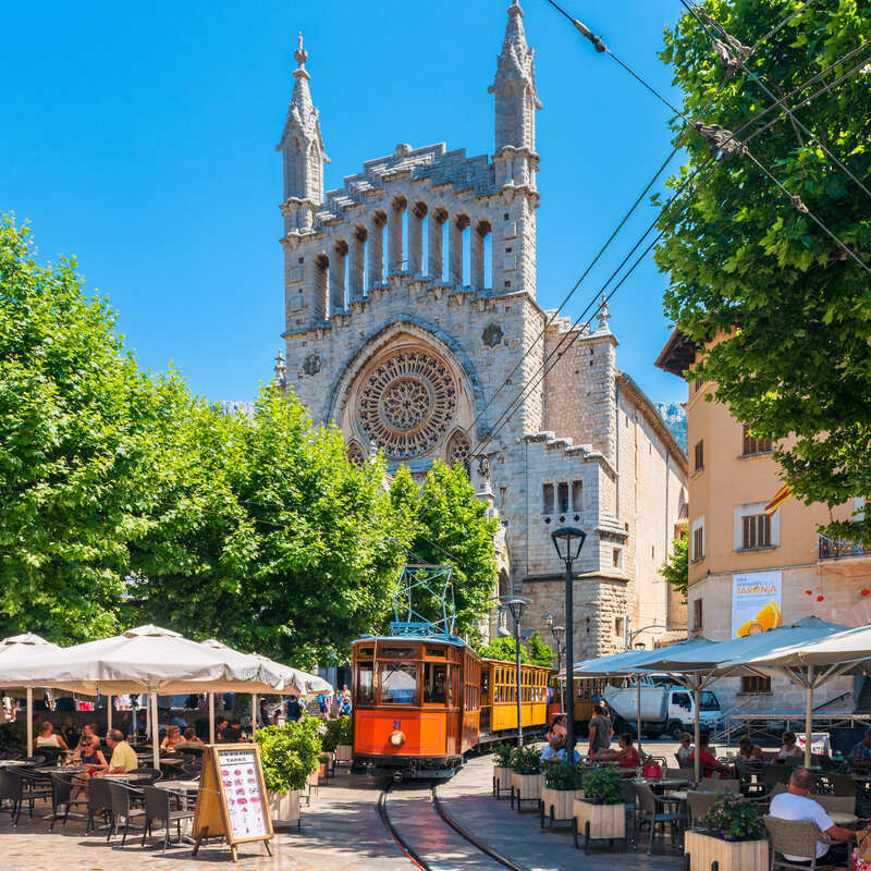 Soller's Heritage Tram Traveling Through The Narrow Streets In Front Of Soller Cathedral, Mallorca, Balearic Islands, Spain, Southern Europe