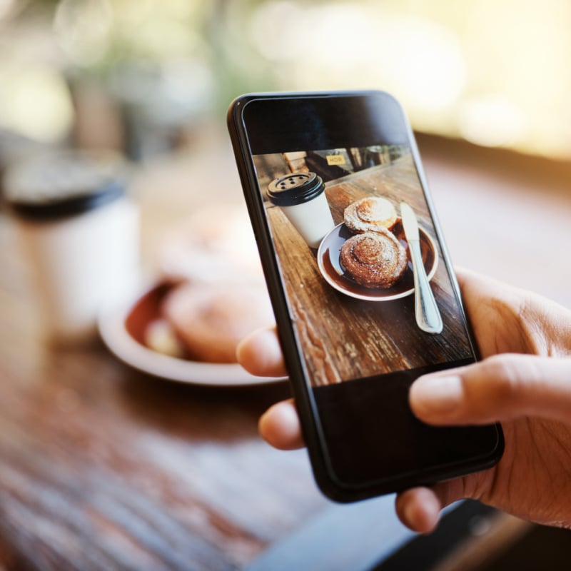 person taking a photo of coffee and danish pastry on a smartphone