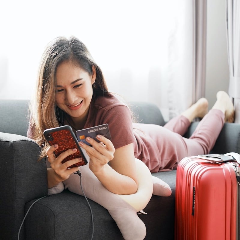 Woman with travel baggage using smartphone booking flight tickets 