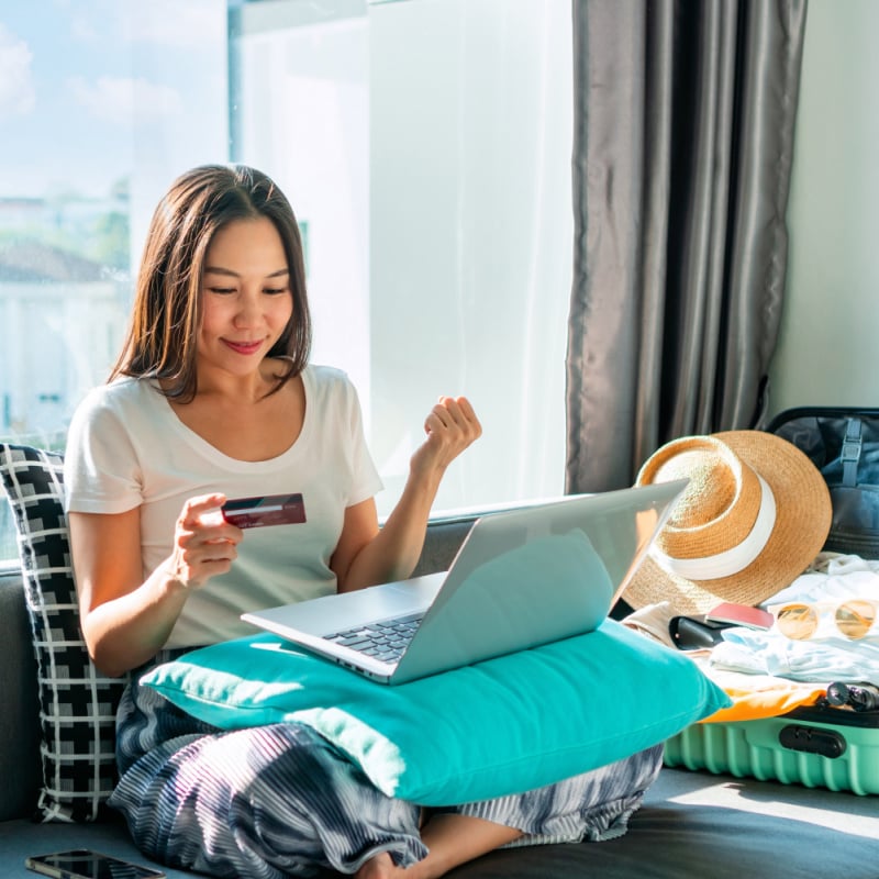 young female traveler booking a flight on her laptop while sitting on a bed