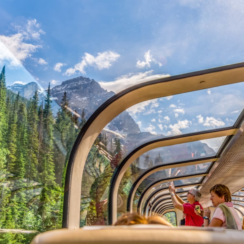 Passengers looking out the glass dome windows on a Rocky Mountaineer train through the Canadian Rocky Mountains