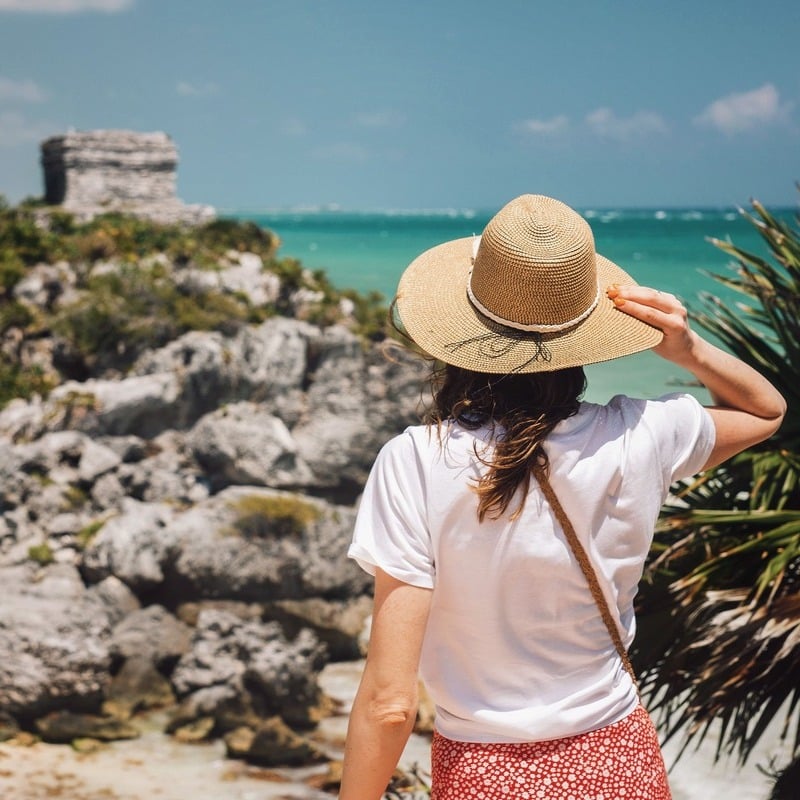 Young Woman Holding A Straw Hat As She Admires A View Of The Tulum Ruins In The Mexican Caribbean, Mexico